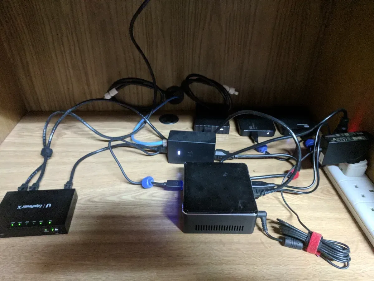 Small computers, power adapters, and network gear arranged on a wooden shelf.