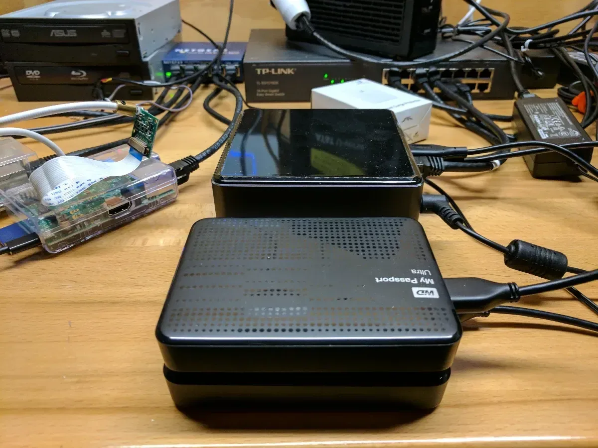 Two compact network devices stacked on a crowded homelab workbench.