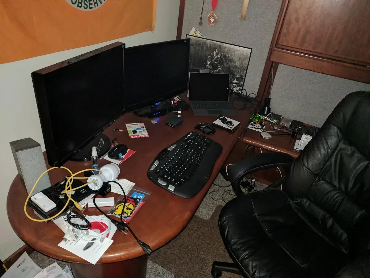 Temporary multi-monitor workstation with homelab equipment spread across the desk.