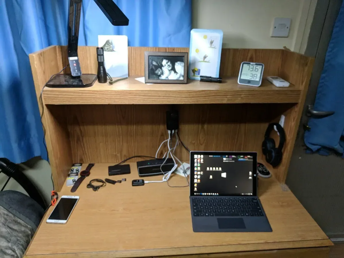 Laptop and compact homelab devices arranged on a desk beneath a shelf.