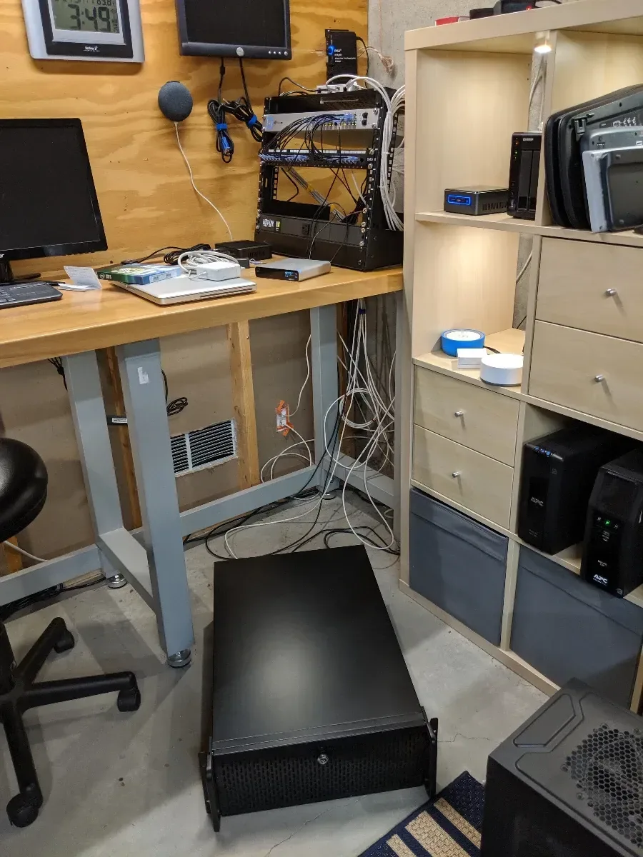 Server chassis on the floor beside the rack and homelab workbench.