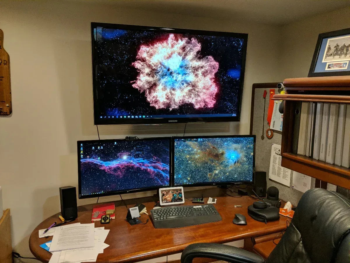 Multi-monitor workstation with a large wall-mounted display above the desk.
