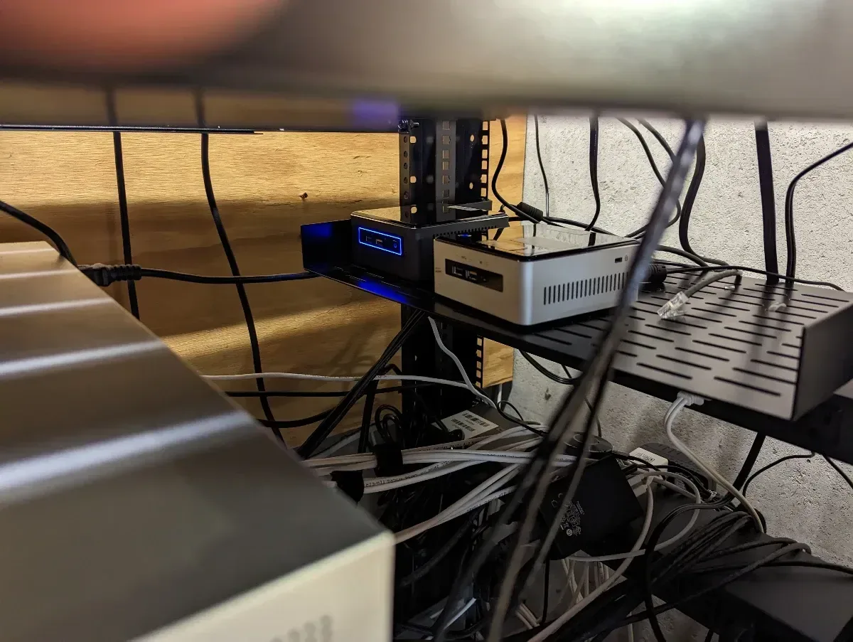 Lenovo Tiny computer mounted beneath a desk among the homelab cabling.