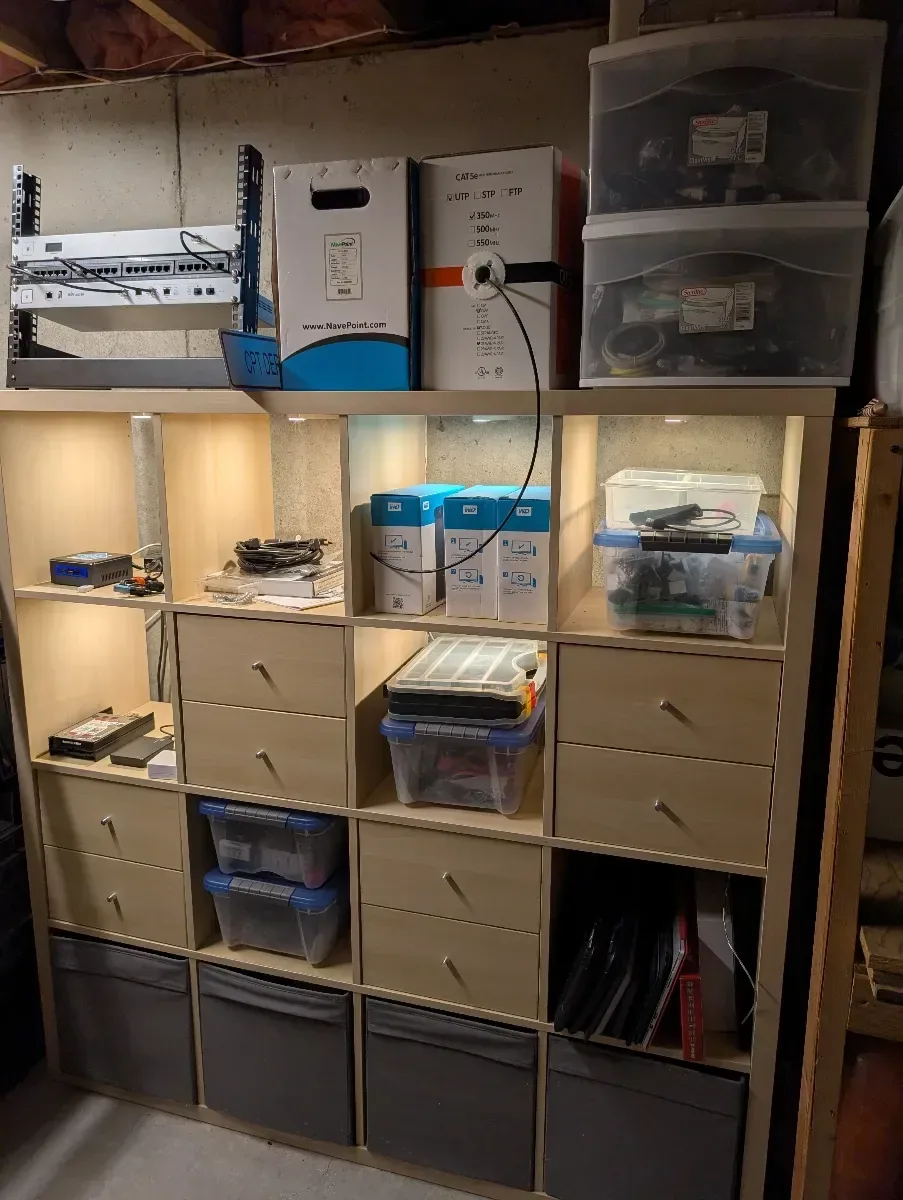 Storage shelves organized with homelab parts, devices, and project bins.