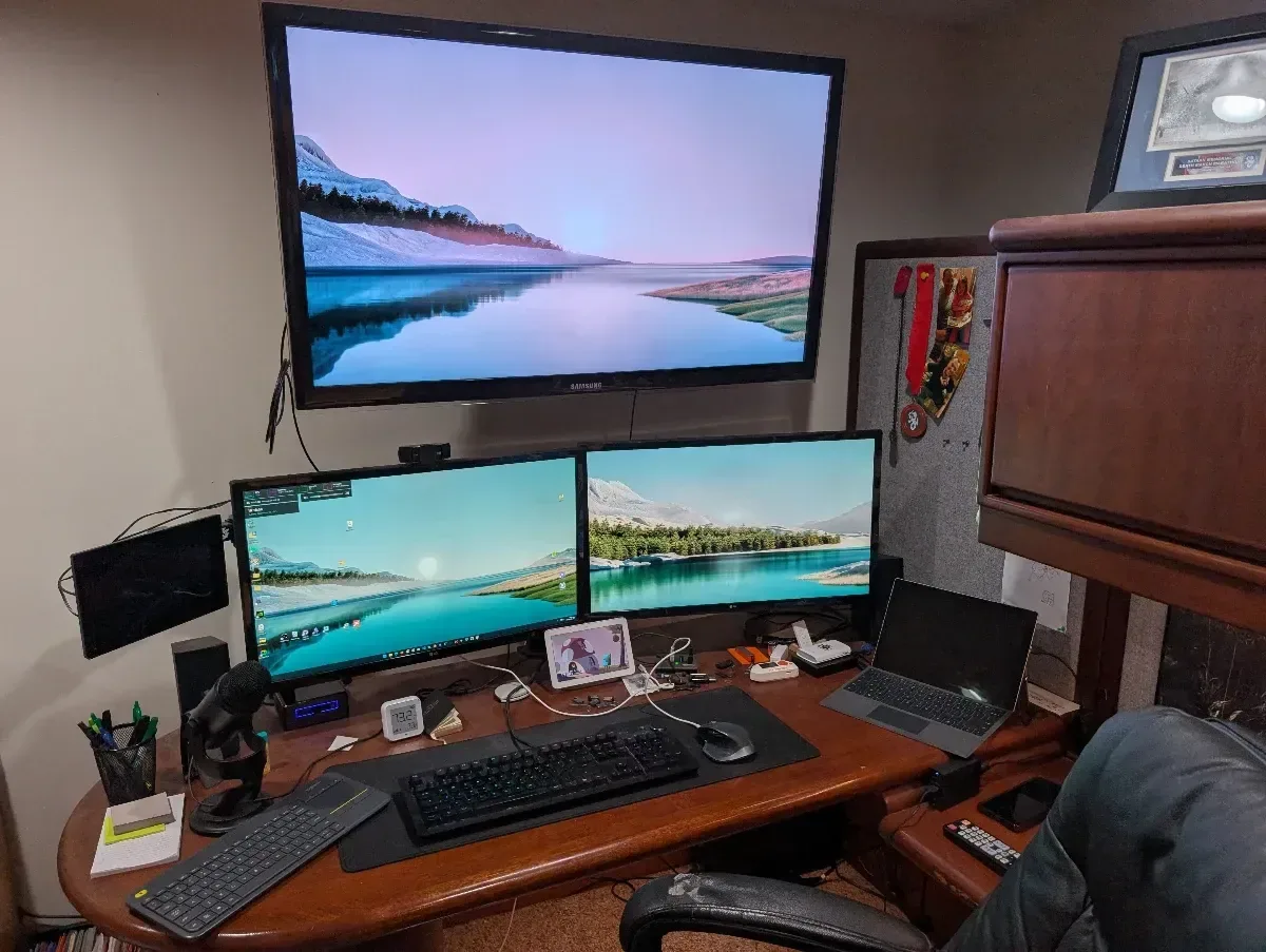 Desk with three monitors and a large wall-mounted display.